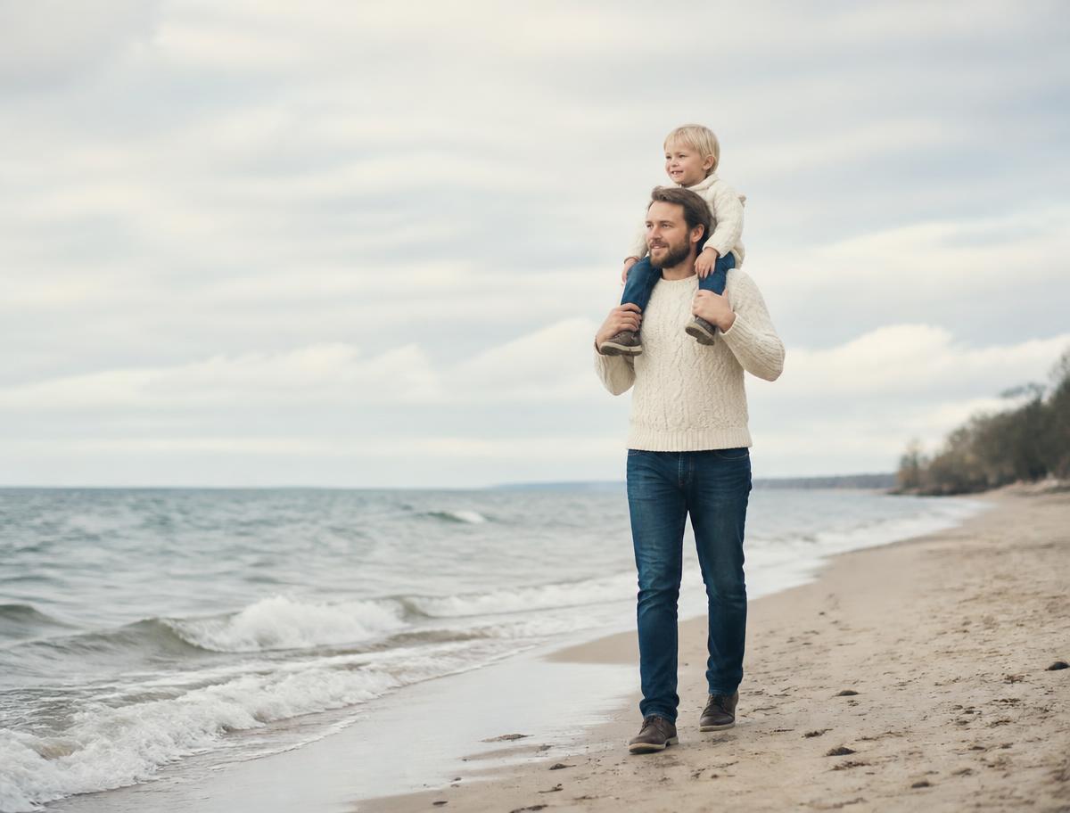 Vater trägt sein Kind auf den Schultern am Strand